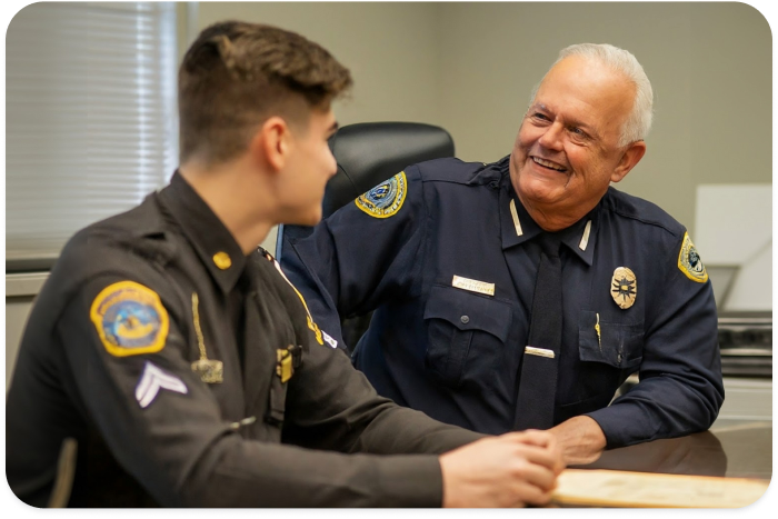 two policemen sitting at a desk and smiling at each other